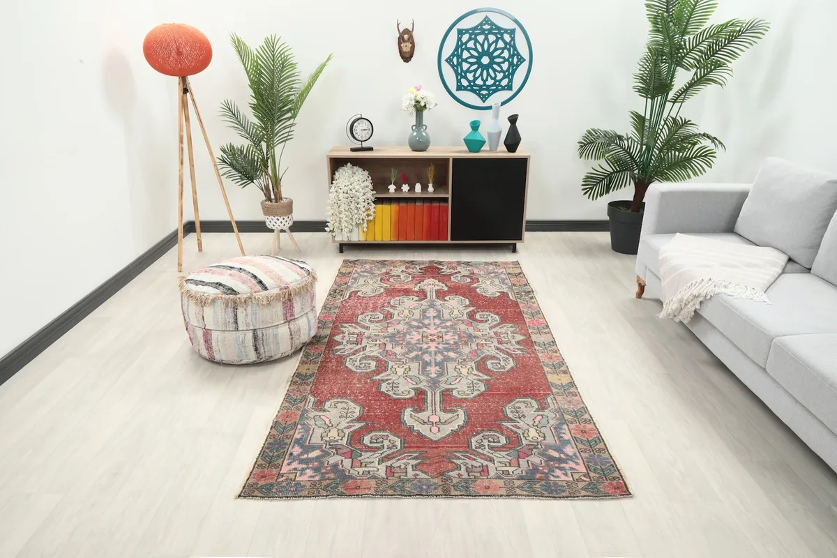 Vintage red tribal rug displayed in a bright living room setup with a sofa and ottoman