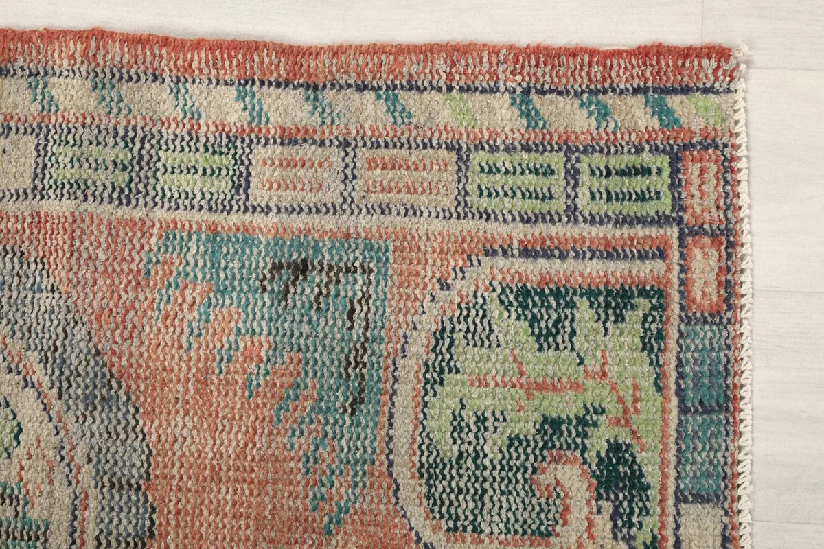 Close-up of the top right corner of the rug, showing the faded rust, blue, and green colors and geometric border.