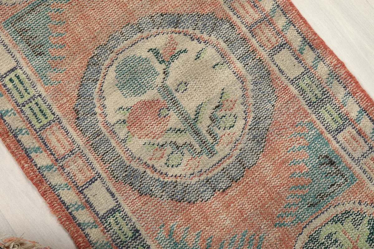 Detail of the central medallion with floral motifs in blue, pink, and ivory against the rust background.