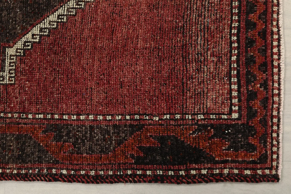 Detailed view of the rug's corner, showcasing the red field, black border, and subtle wear