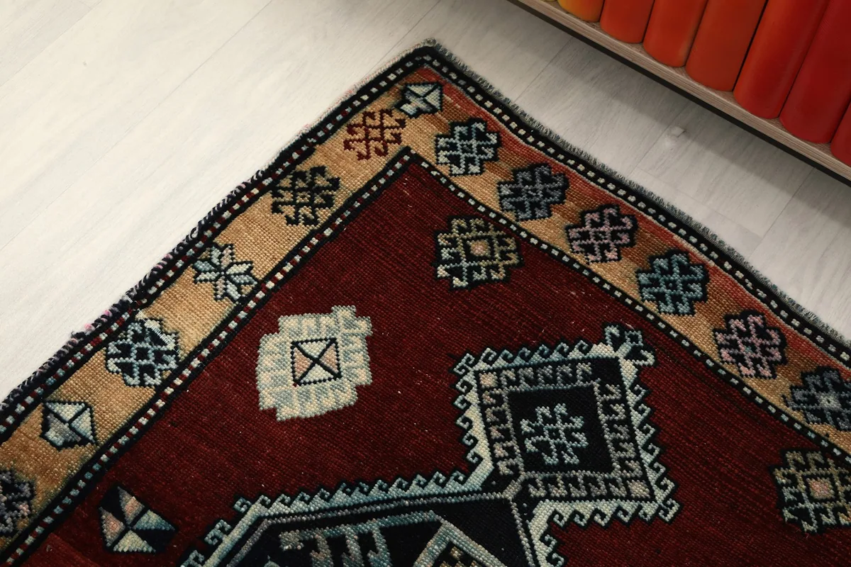 Close-up of a rug corner, highlighting the tan border with small geometric patterns and the rust field.