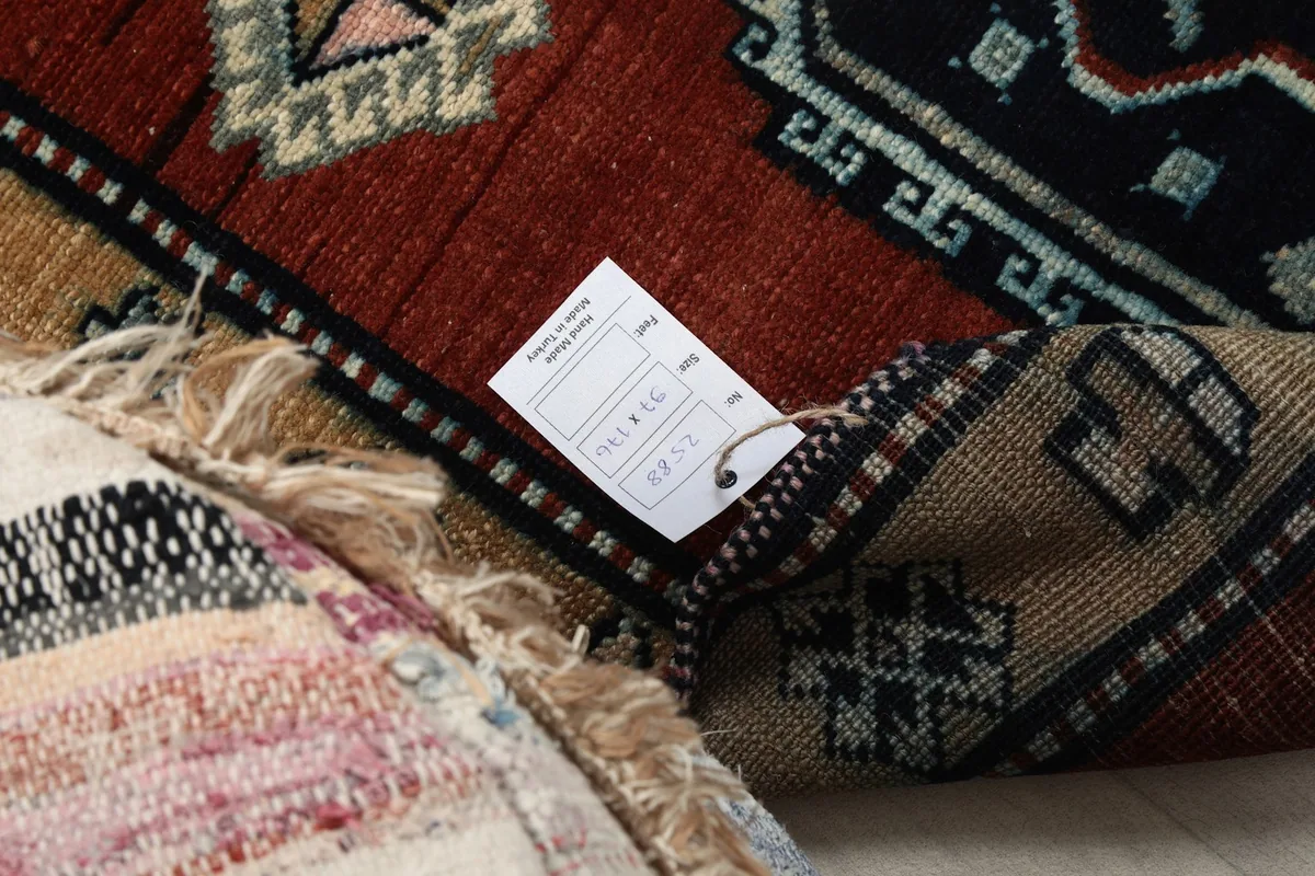 Close-up of the rug's fringe and a corner, showing the wool texture and a product tag.