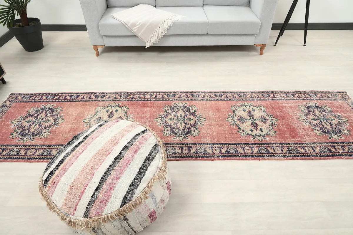 Long shot of the rose geometric runner rug in a room with a sofa and a decorative pouf.