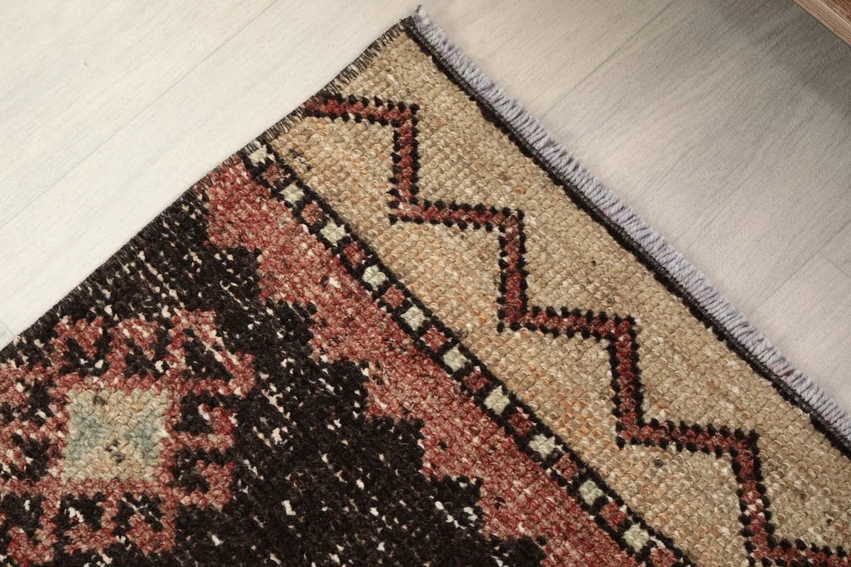 Detail of the rug's end border and fringe, showing the beige zigzag pattern and slight wear