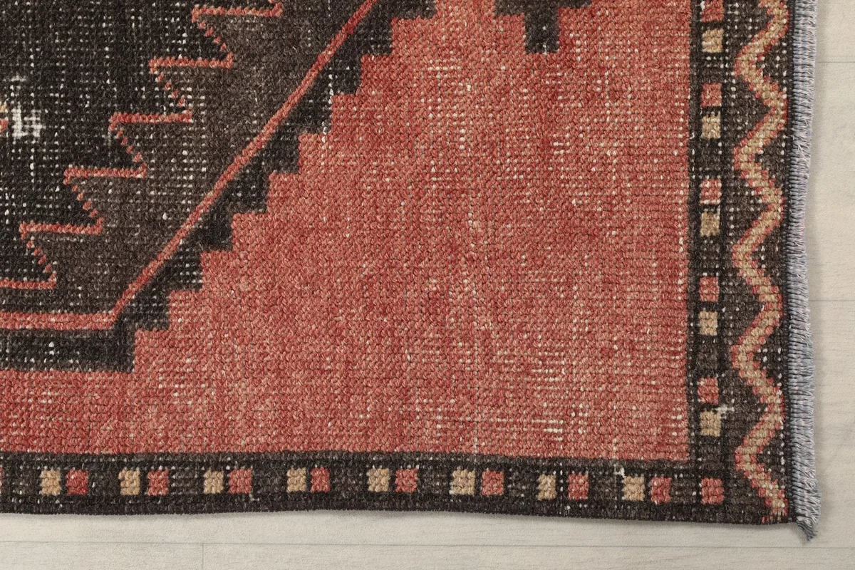 Detailed view of the rug's border and a section of the rust field, showing subtle patina.