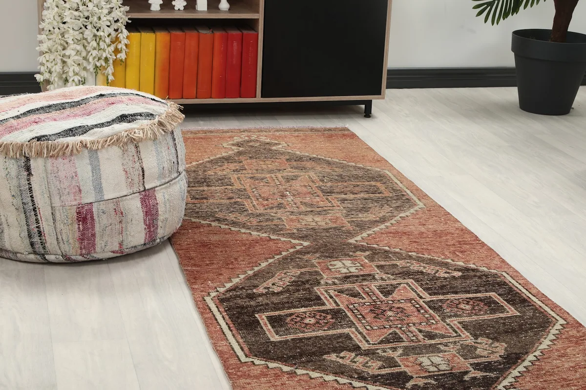 Close-up view of the runner rug in a room, showing its rust and brown tribal patterns next to a pouf