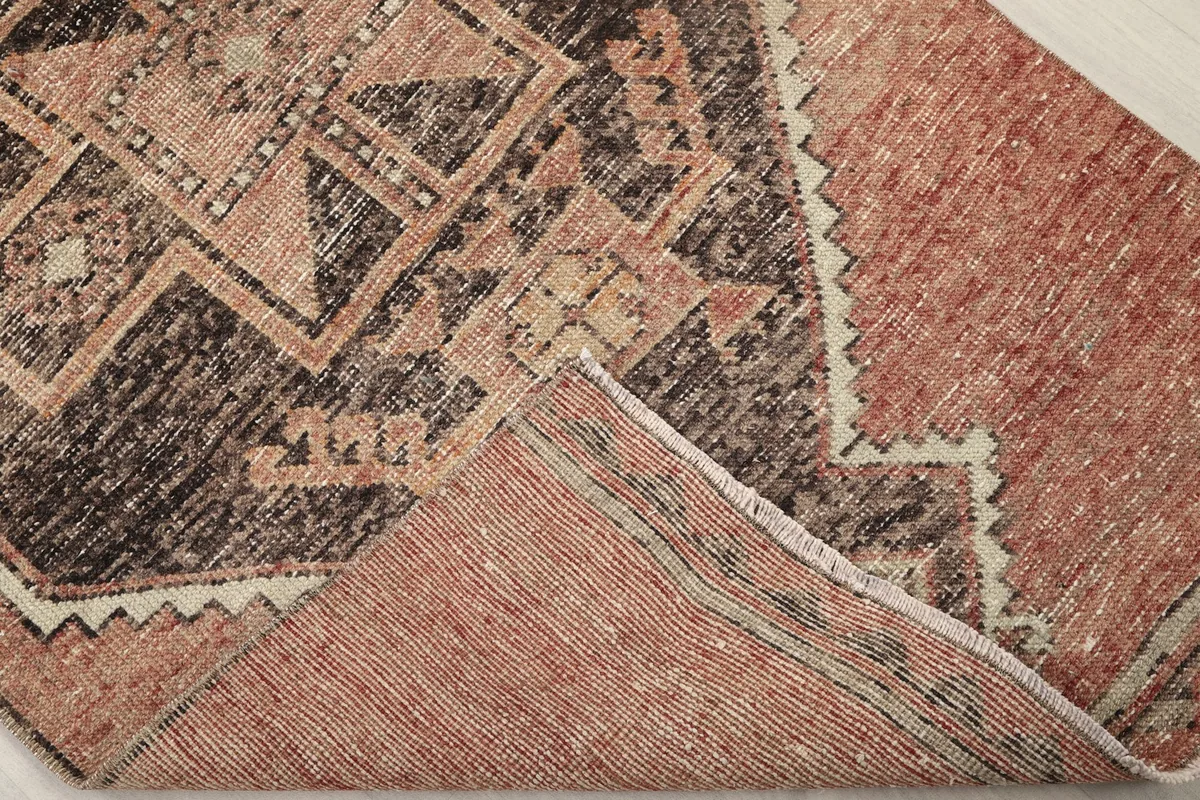 Corner of the rug folded back, showing the cotton foundation and reverse side of the hand-knotting