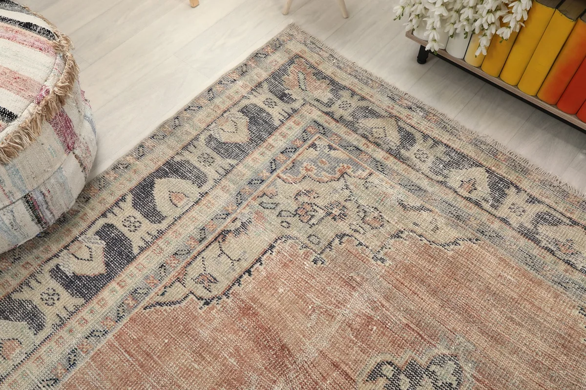 Corner detail of the rug, showing the intricate border design and the faded rust field.