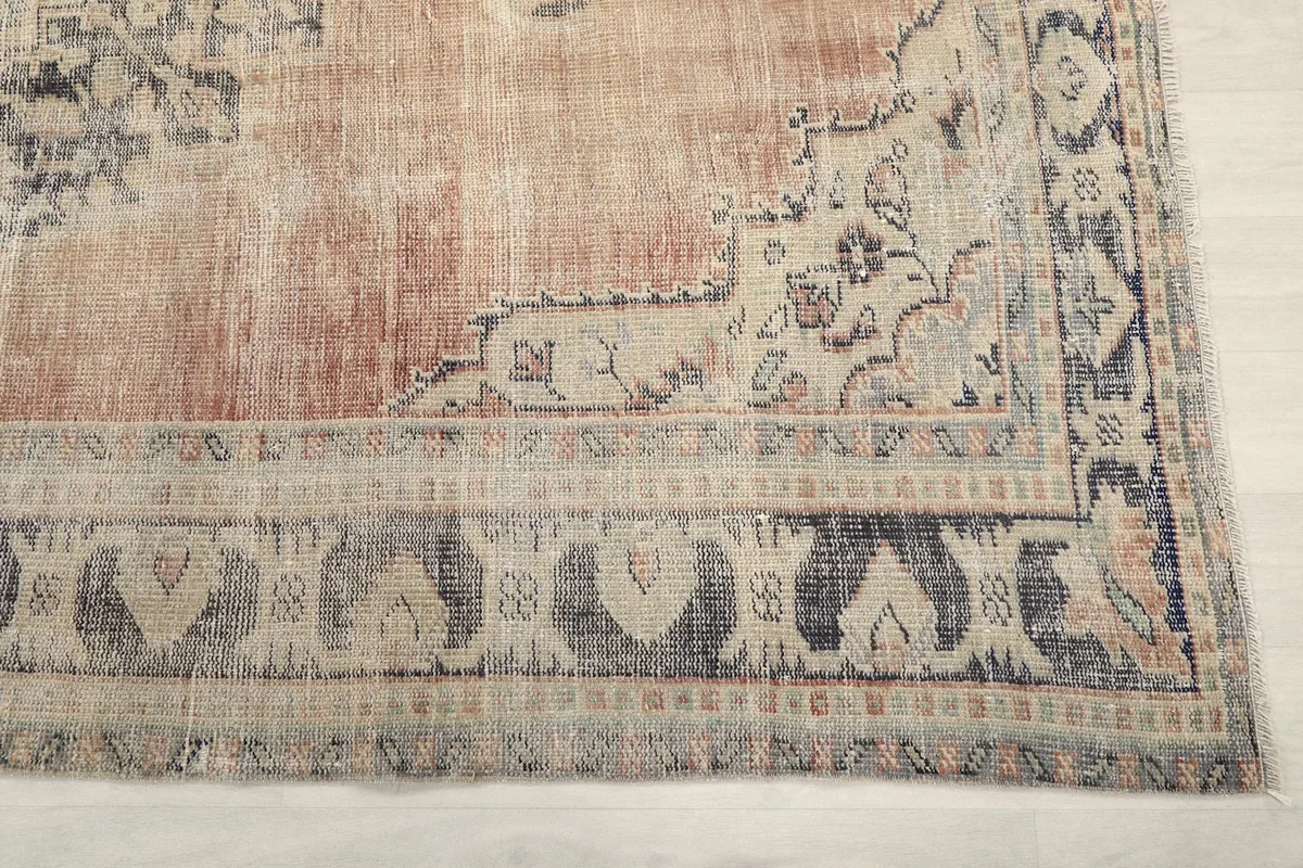 Detail of the rug's border pattern in blue, gray, and beige, with a corner of the main rust field.