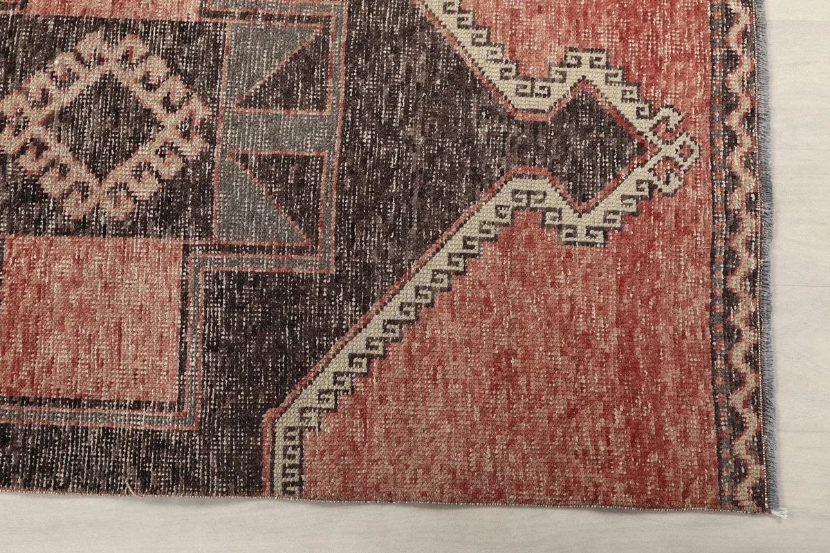 Detailed view of the rug's border and a section of its rust-colored field with subtle wear