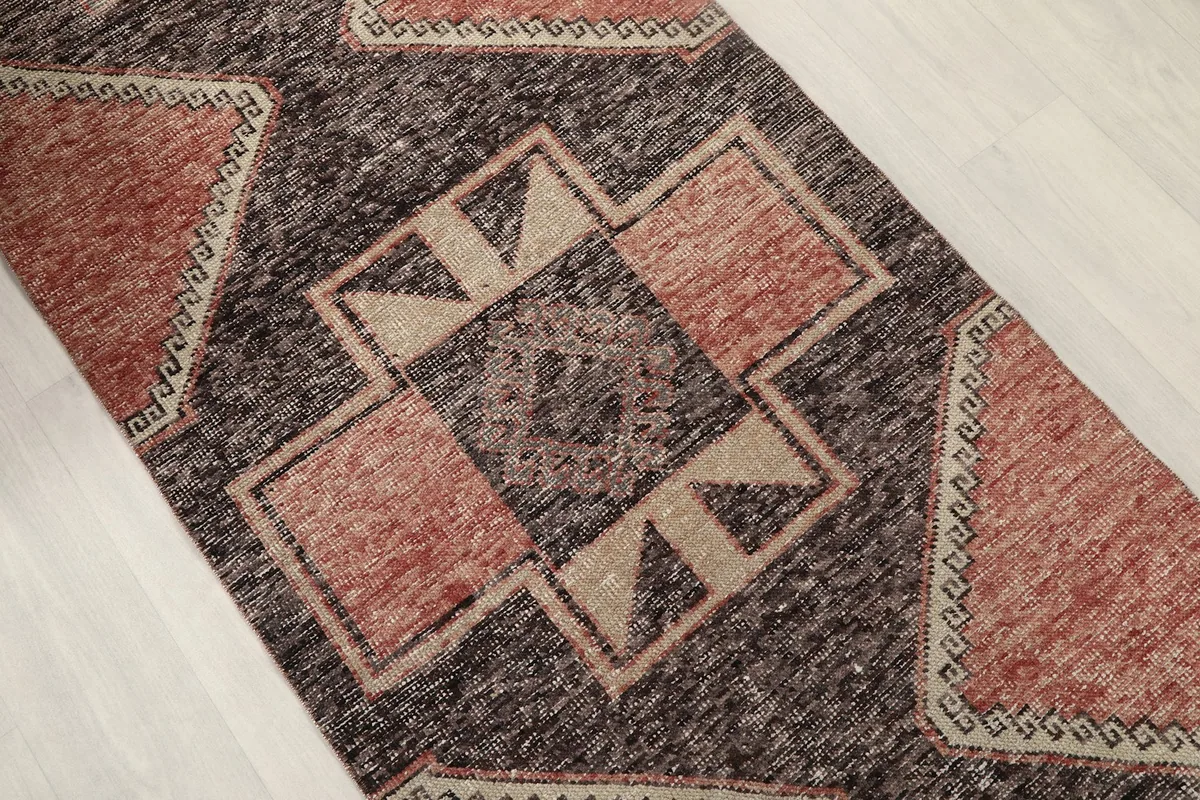 Close-up of a central geometric motif in charcoal, rust, and beige, showing the hand-knotted texture