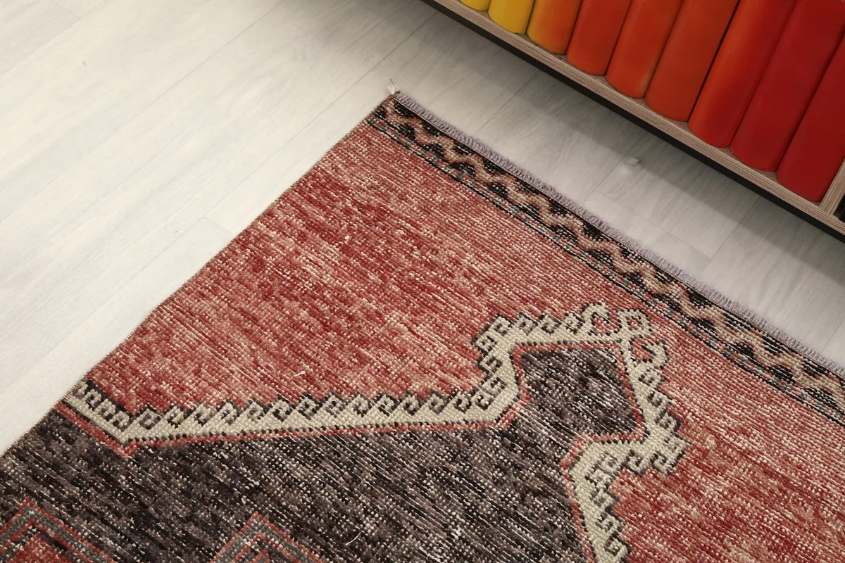 Detailed view of the rug's end border and a corner of the rust field, showing the subtle color variations
