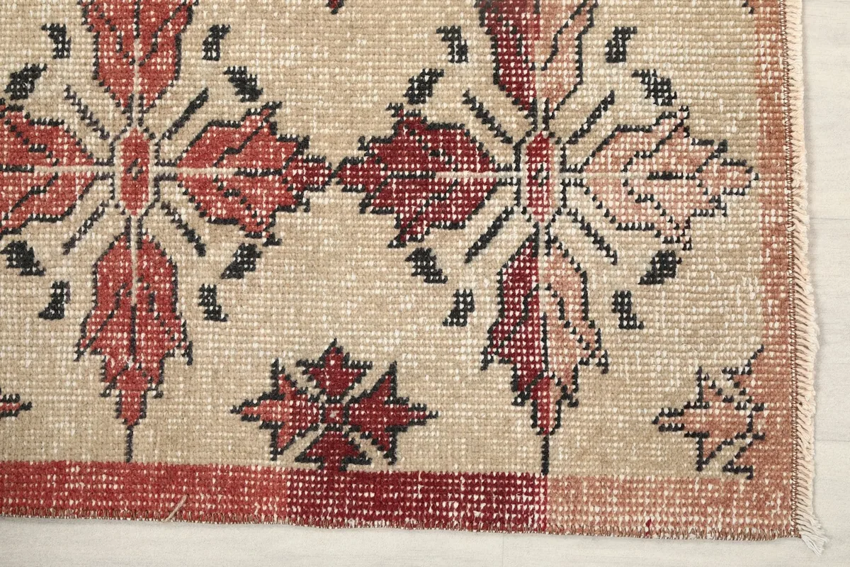 Detailed corner of the rug showing the rose border and beige field with motifs
