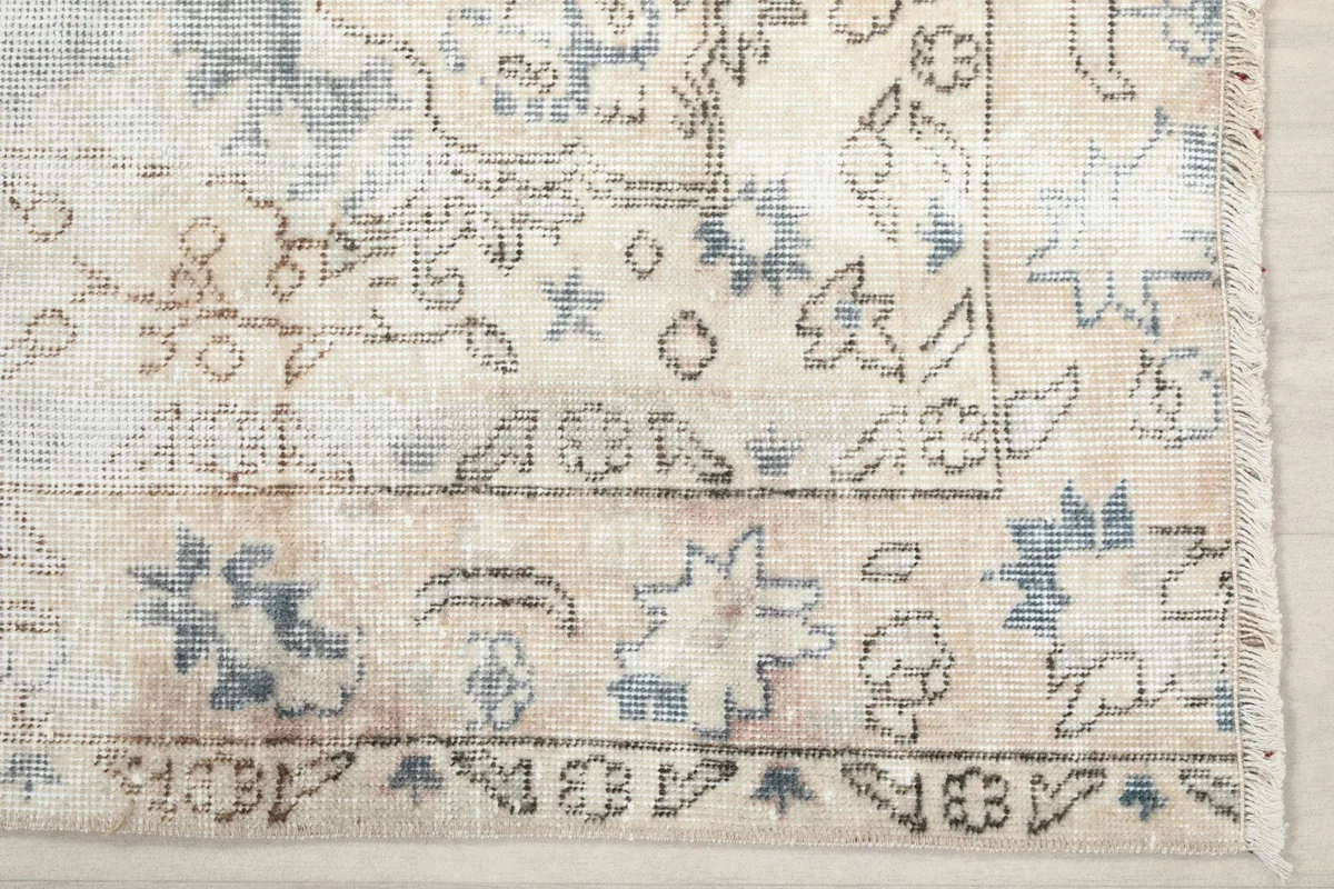 Detail of the rug's border, featuring faded beige and blue floral patterns on a light background