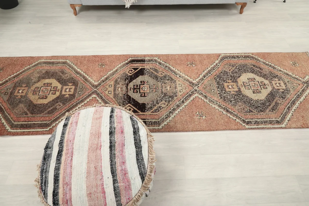 Full length view of the runner rug on a light floor, with a striped pouf in the foreground.