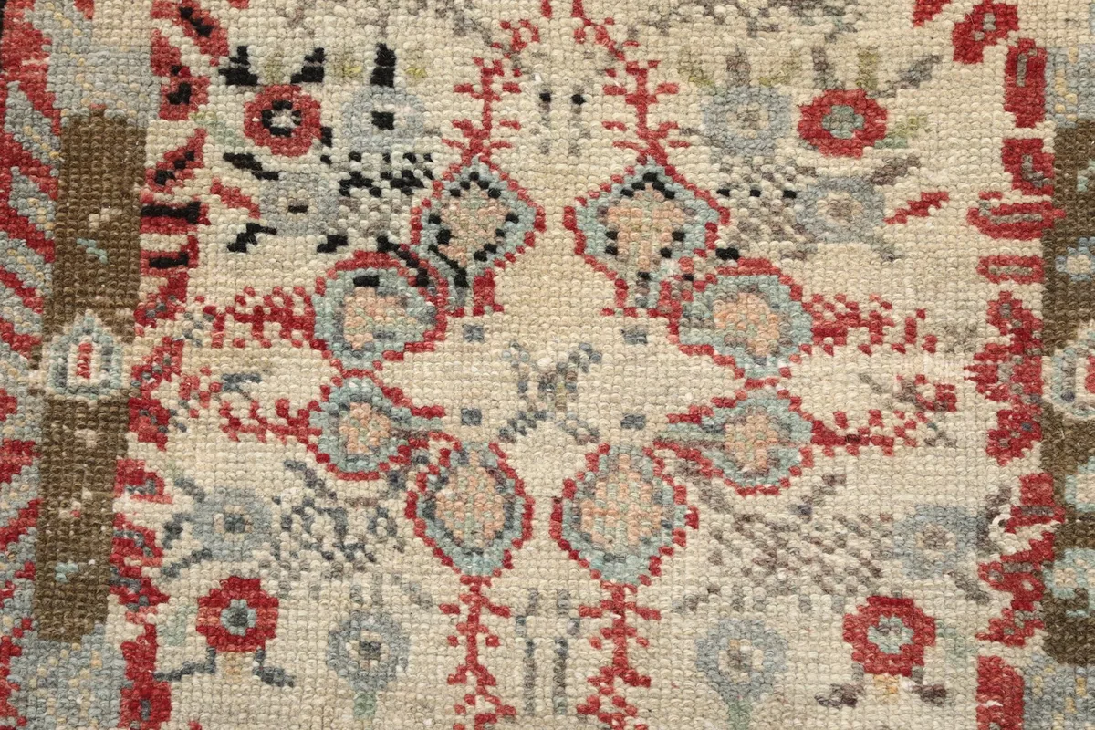 Macro view of the hand-knotted wool pile, showing specific motifs within a medallion with red, gray, and tan threads