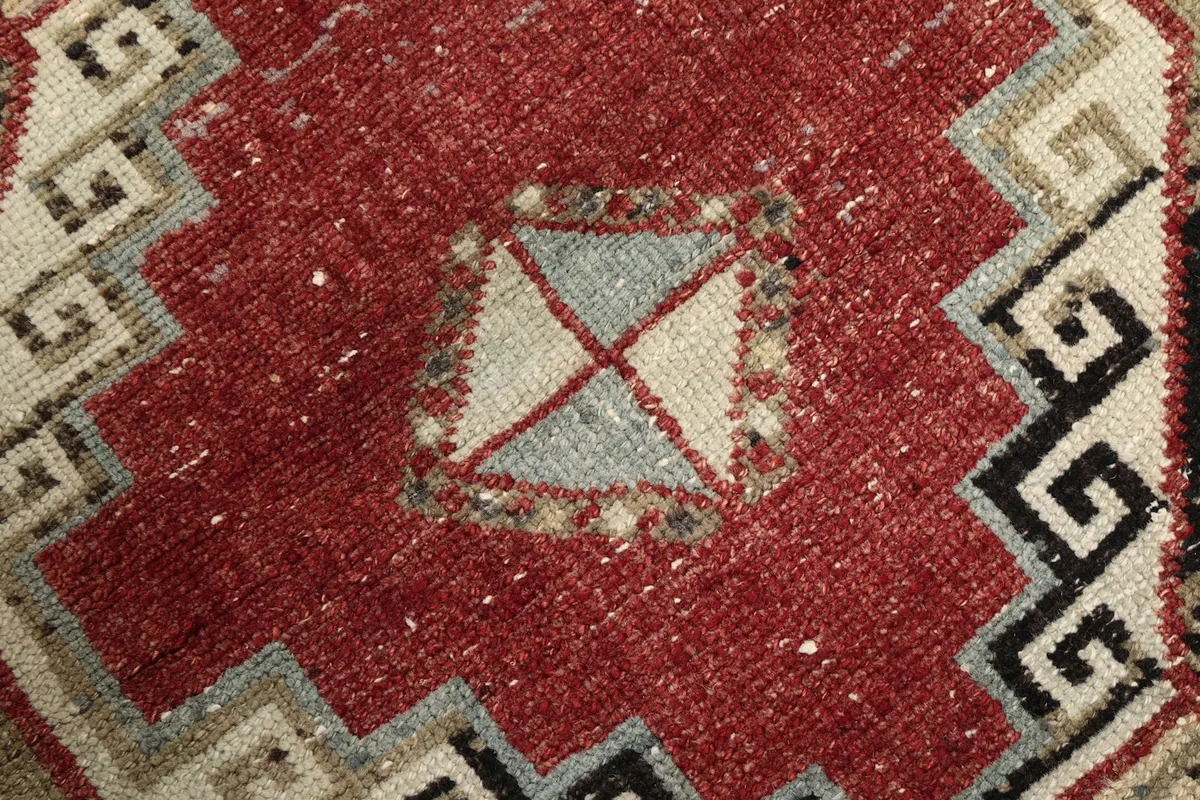 Close-up of a red geometric medallion with gray and beige accents, showing wool texture