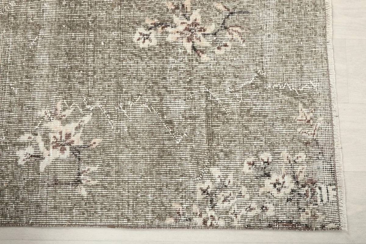 Close-up detail of the faded floral motifs and distressed gray pile near the edge of the rug.