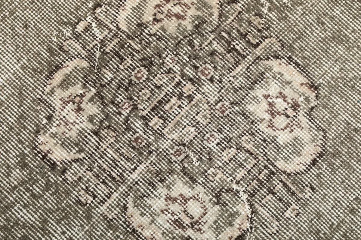 Extreme close-up of the low pile and intricate, faded details of the hand-knotted wool on cotton rug.