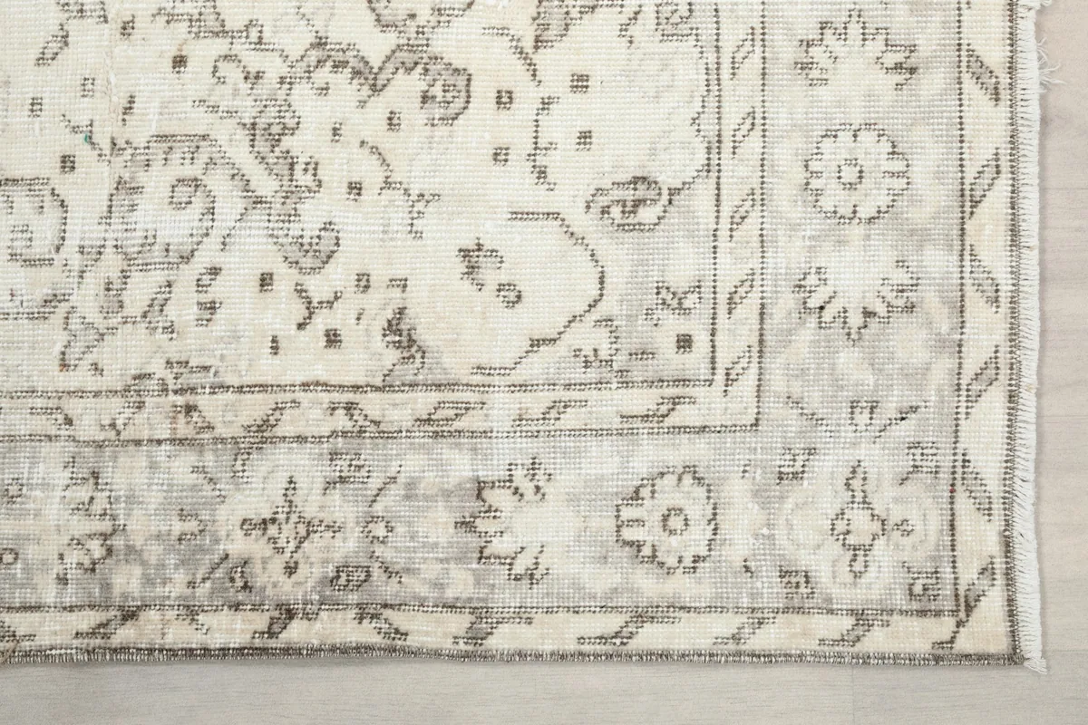 Detailed view of the rug's corner and border design, highlighting the gray floral motifs against the cream field.