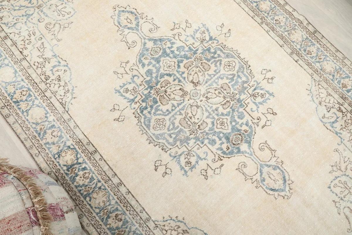 Angled view highlighting the central blue medallion and faded ivory field of the rug.