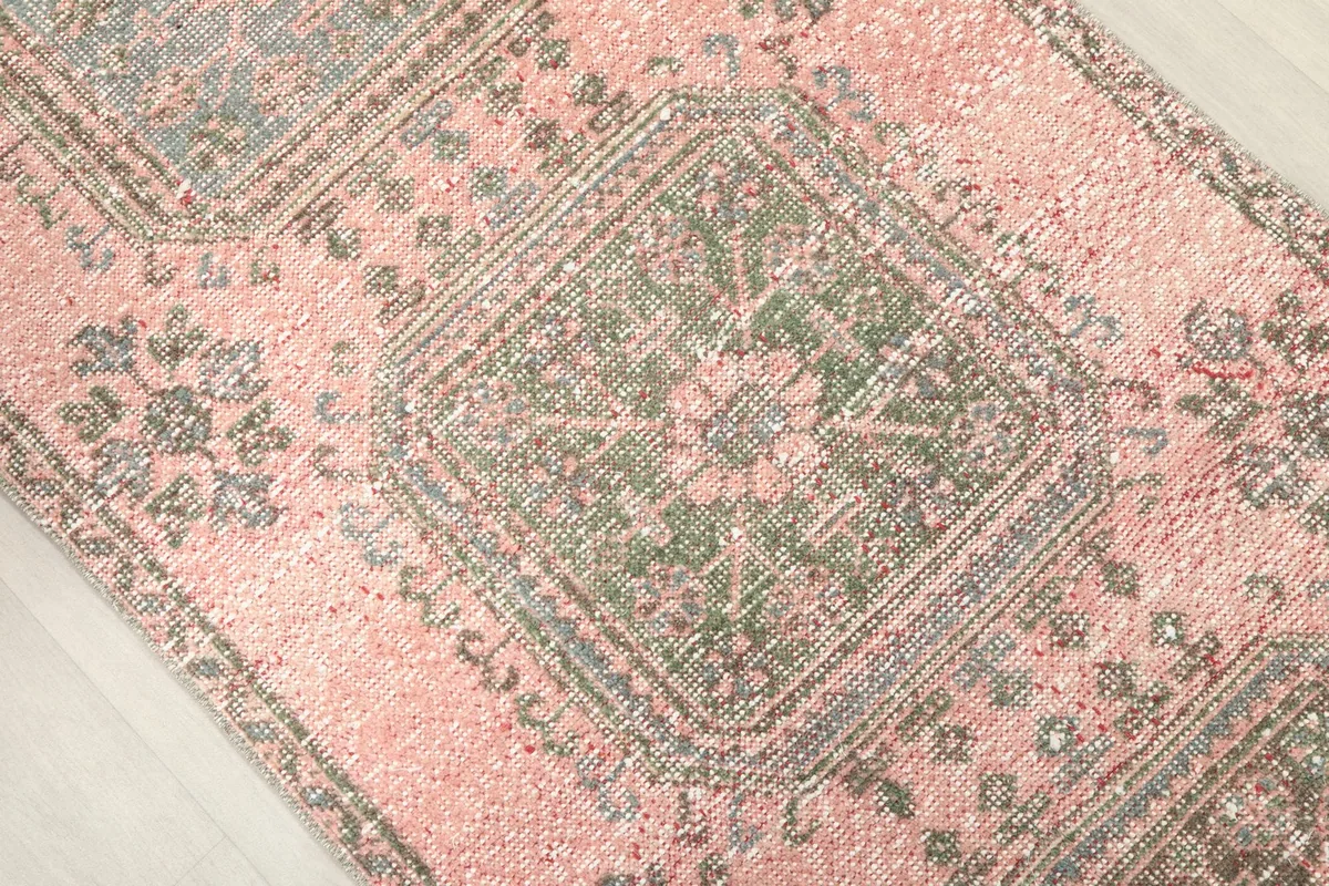Overhead close-up of a geometric medallion with olive and gray tones on the rose background.