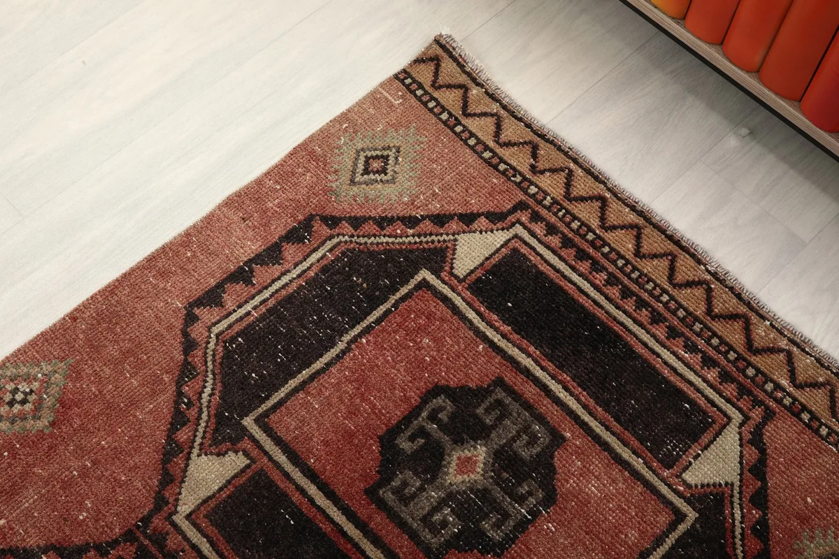 Corner detail showing the patterned border and the faded rust field of the runner