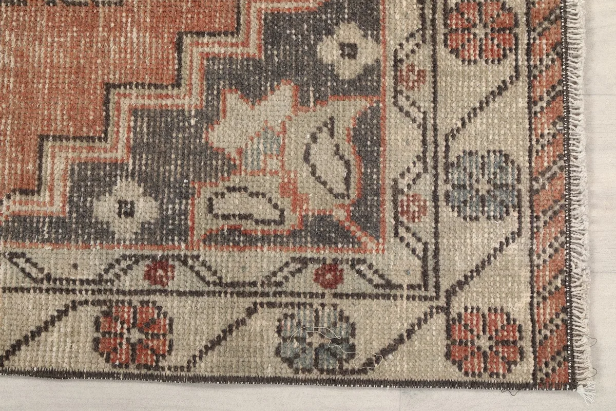Detailed view of the rug's border and corner motifs, showing rust and gray patterns