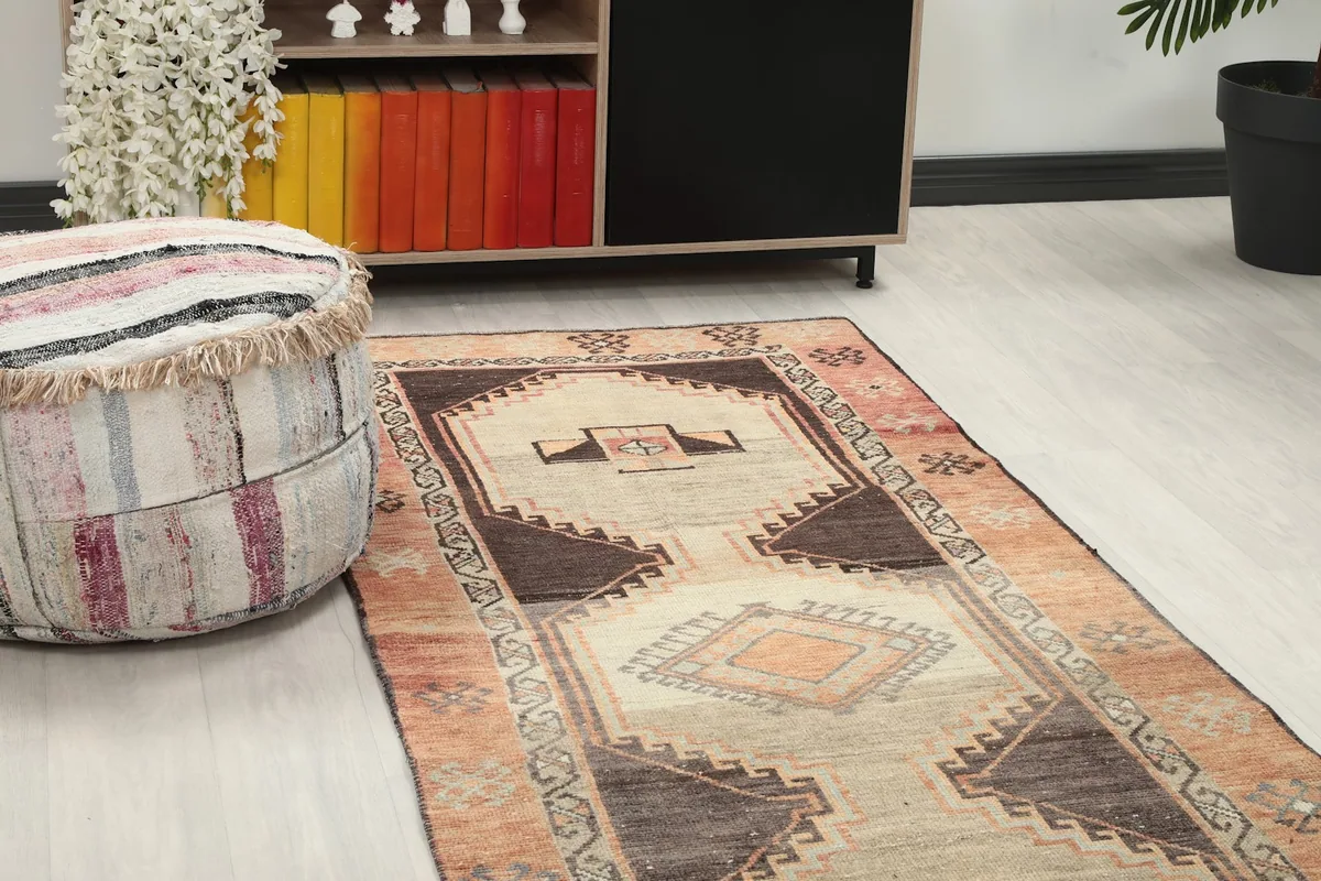 Close-up angle showing the rug's rust border and central tan field next to a pouf