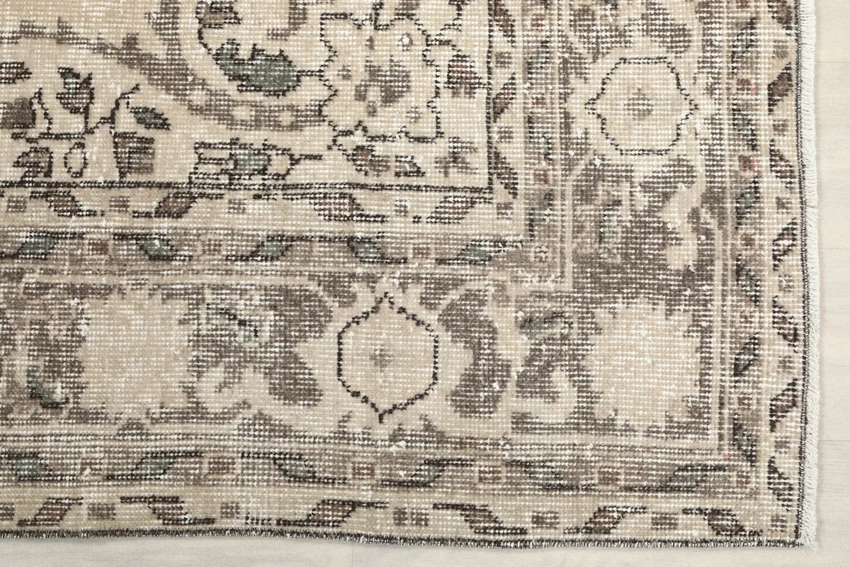 Detail of the rug's intricate border pattern and corner design, showing subtle wear.