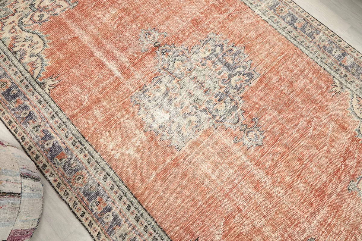 Angled view highlighting the central blue medallion and faded rust field of the rug