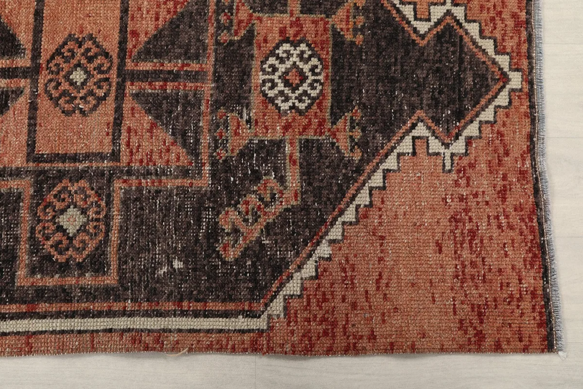 Close-up detail of the rug's corner, showing the rust field and part of a charcoal geometric motif