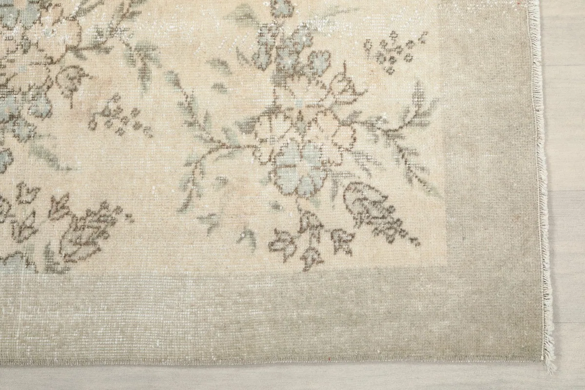 Detail of the rug's border and corner, showing the subtle tan color and floral motif
