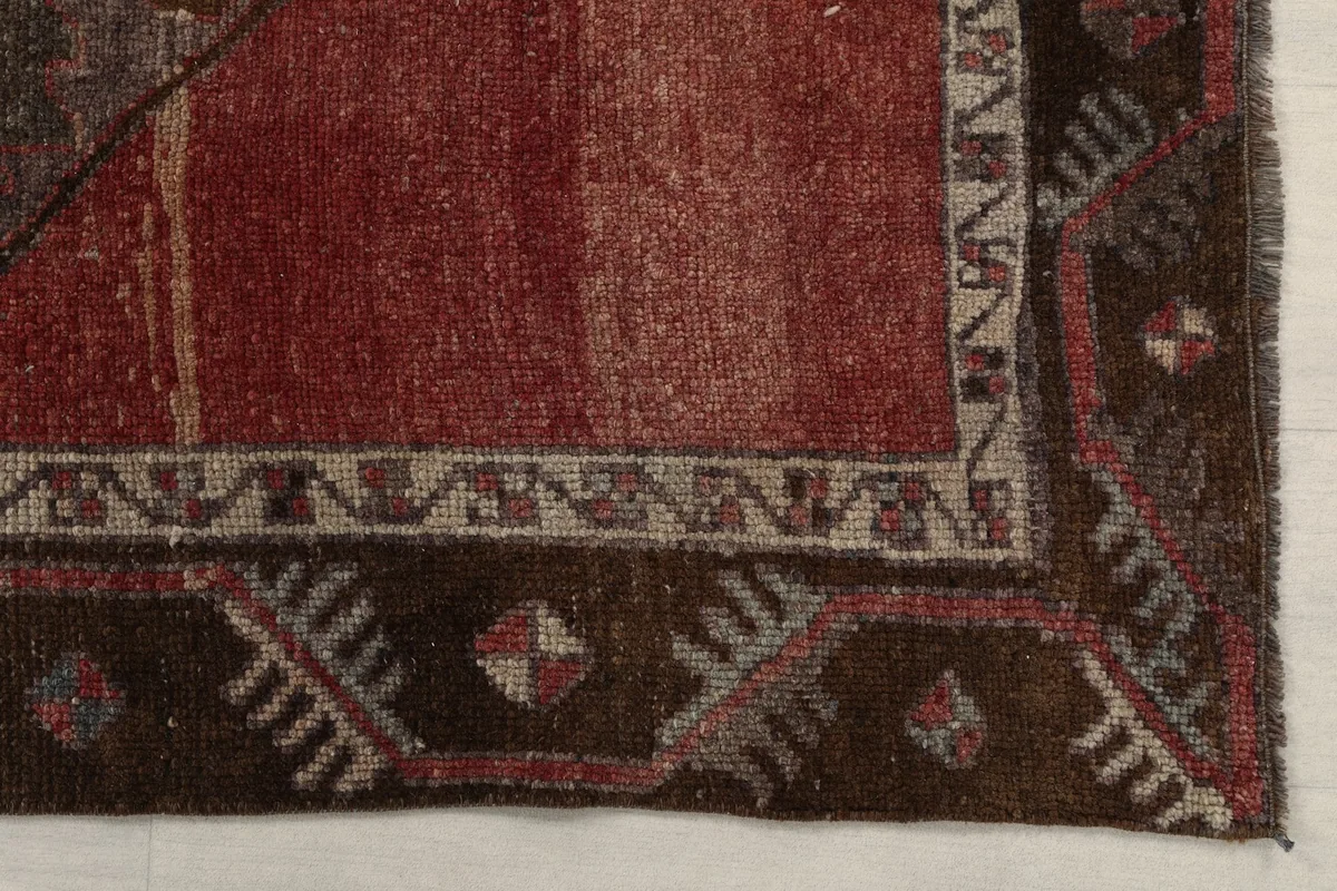 Detailed view of the rug's corner, showing the brown border with geometric motifs and red field
