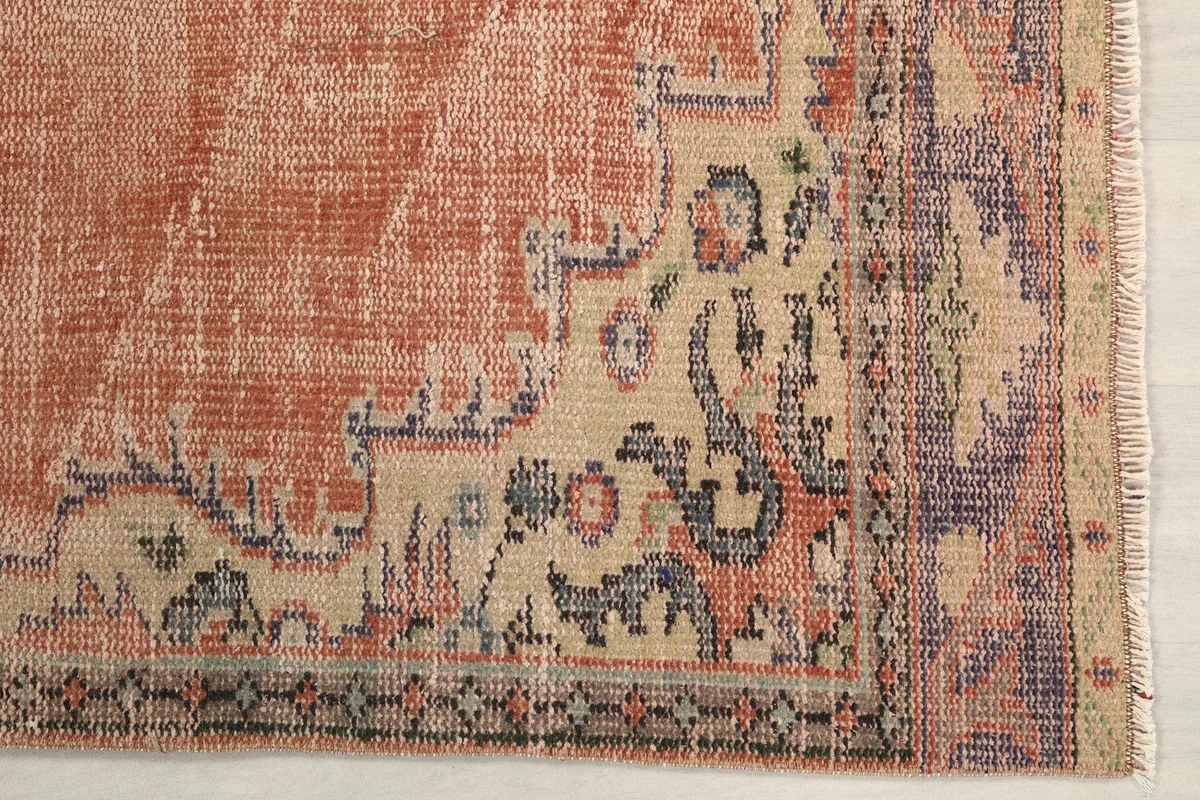 Detailed view of the rug's border and corner, showing faded ivory and purple patterns