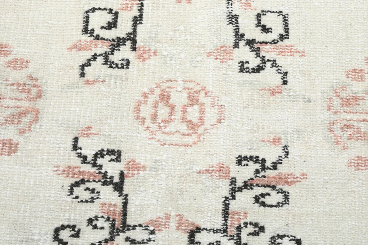 Detailed view of the low wool pile and intricate hand-knotted patterns in ivory, rose, and black.