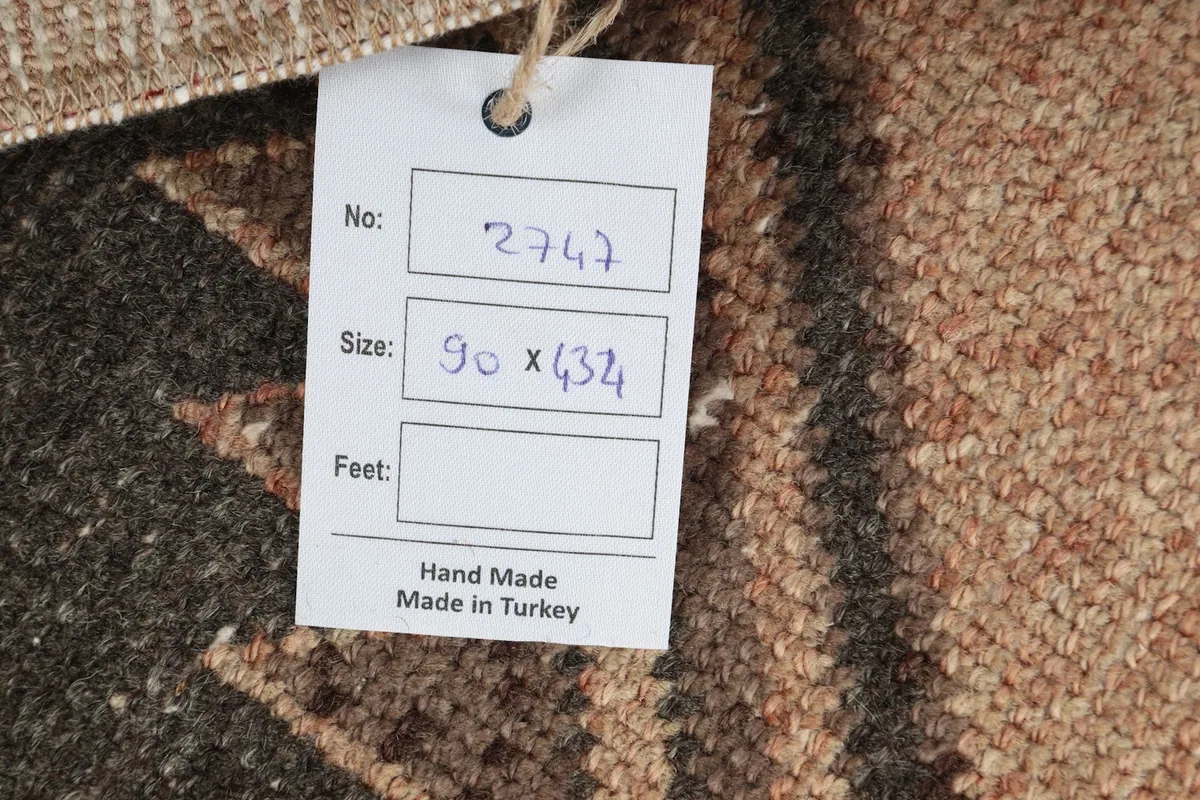 Close-up of the rug's tag, indicating its size as 90 x 434 cm and origin as handmade in Turkey.