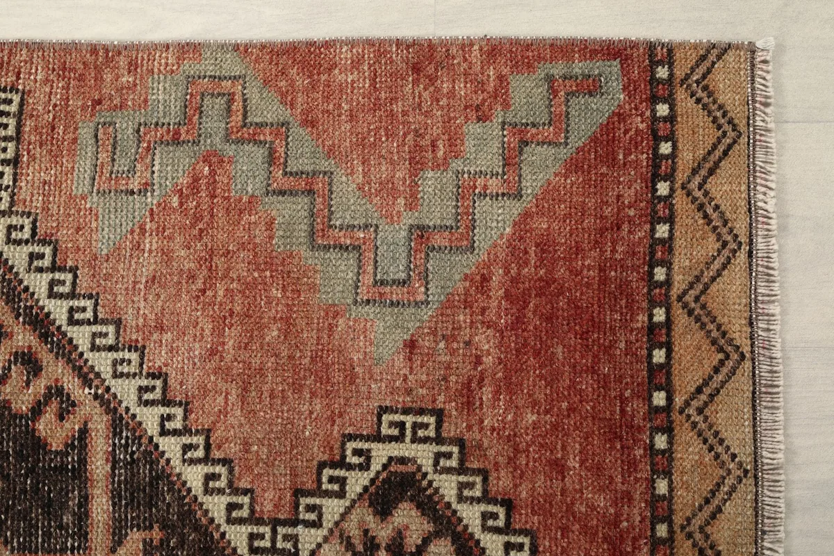 Detailed view of a rust-colored section of the rug with gray geometric motifs and a patterned border