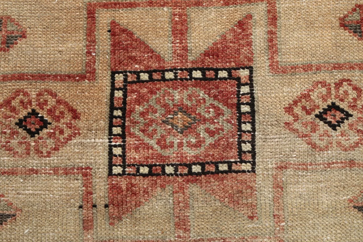 Detailed view of the wool pile texture and a small geometric motif within a beige field