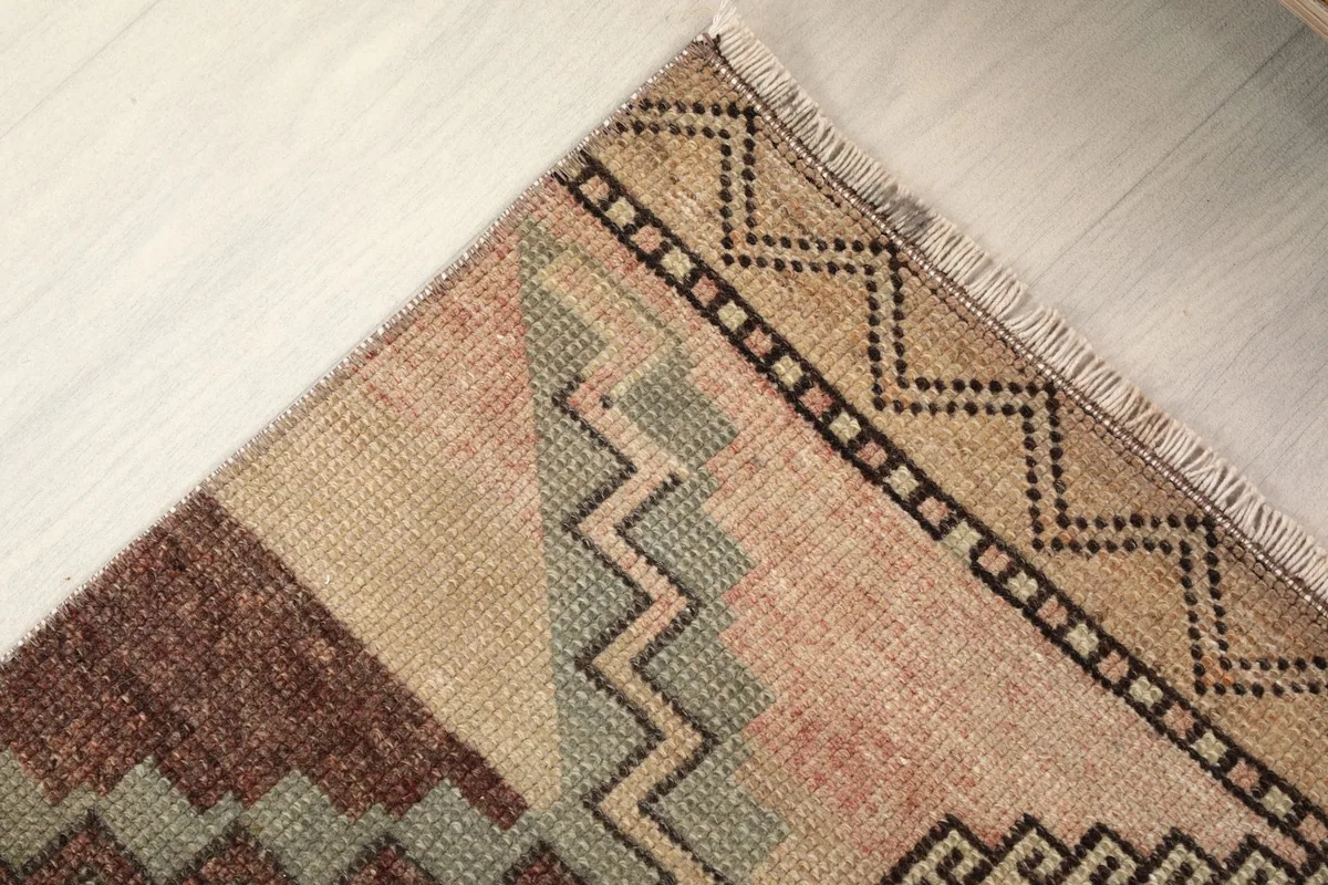 Corner detail showing the patterned border, fringe, and a section with gray and pink tones