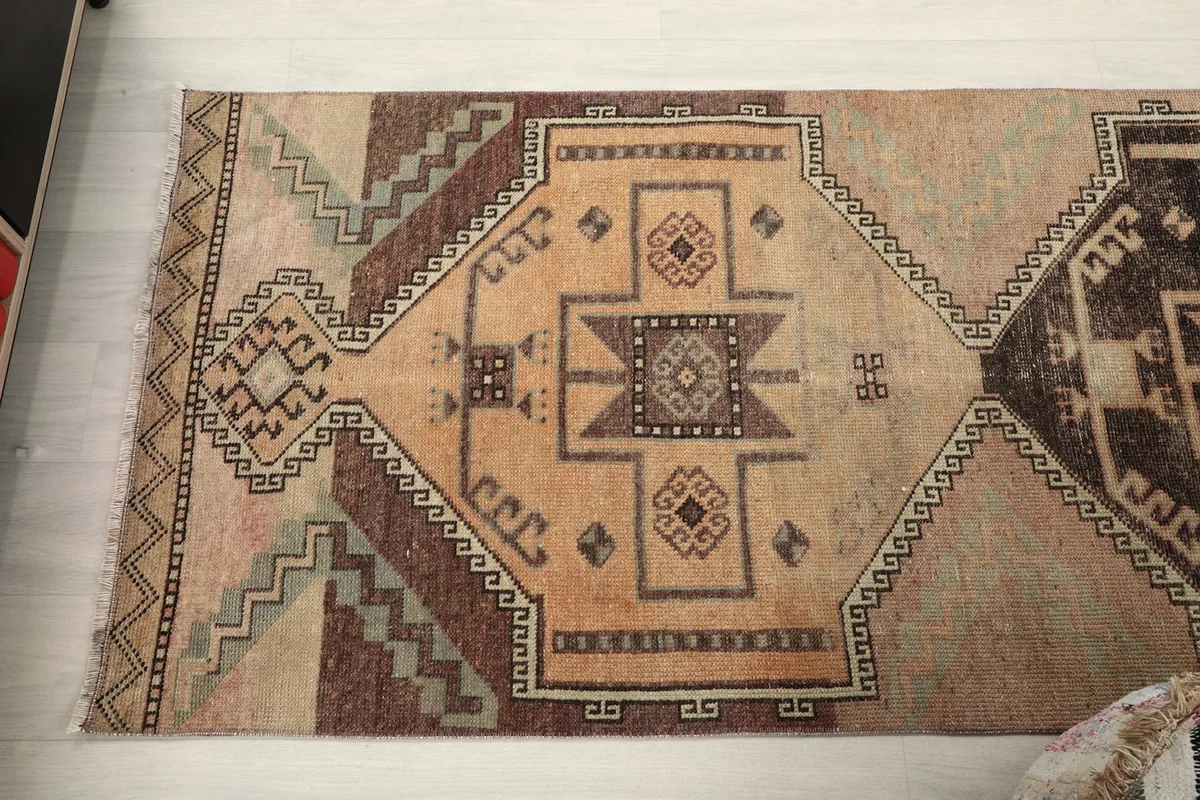 Overhead view of one end of the rug, displaying a beige and brown geometric medallion and surrounding patterns
