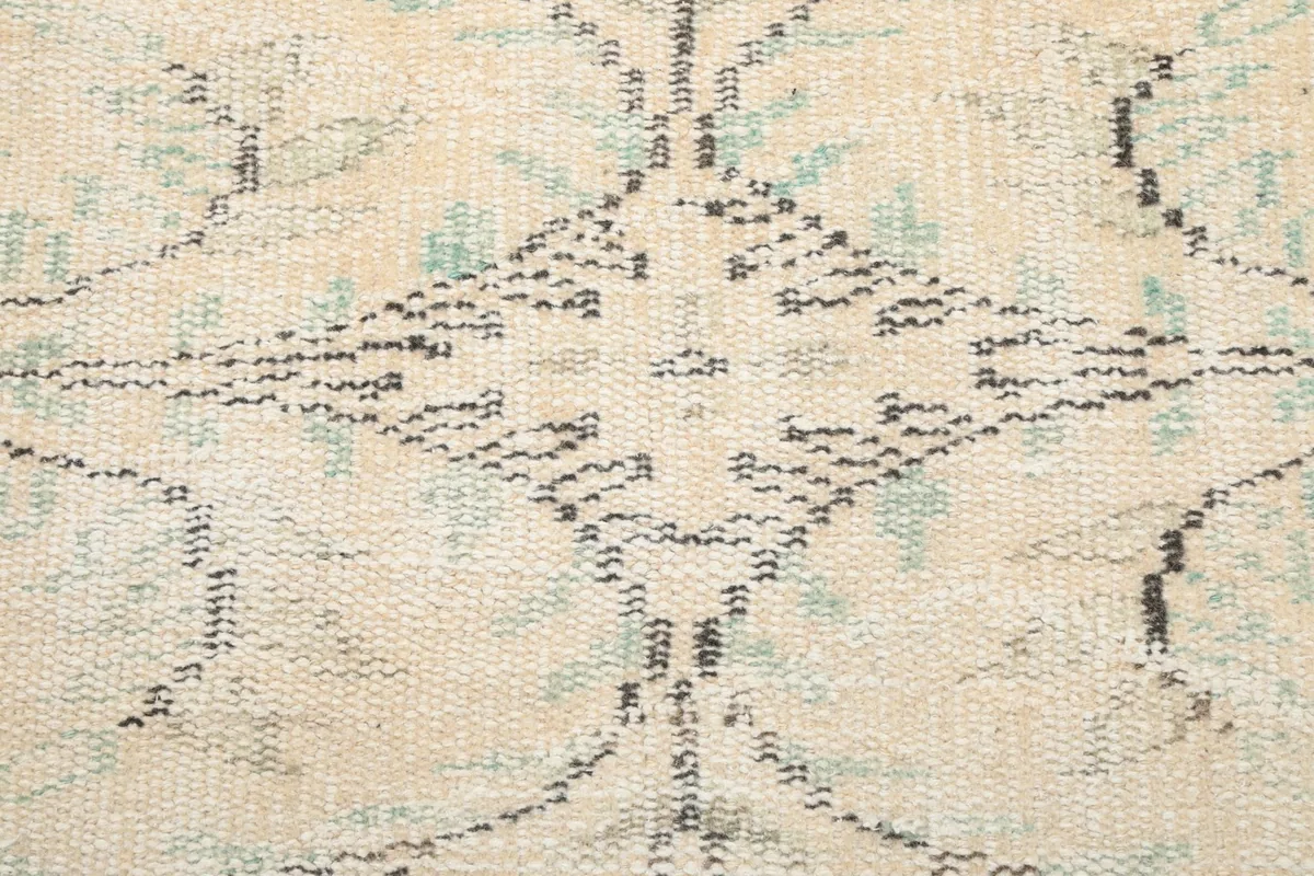 Extreme close-up of a faded geometric pattern within the rug's design, showing individual knots.