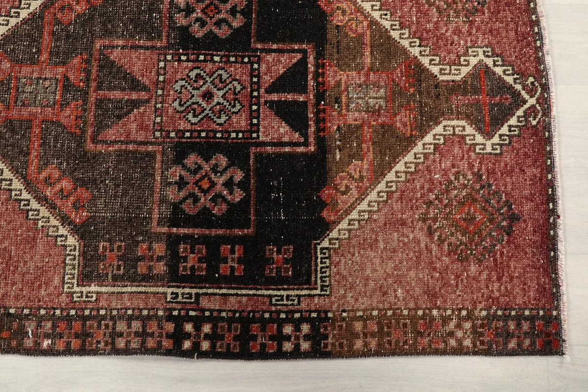 Close-up detail of the rug's central geometric motifs and border patterns in rose, brown, and black