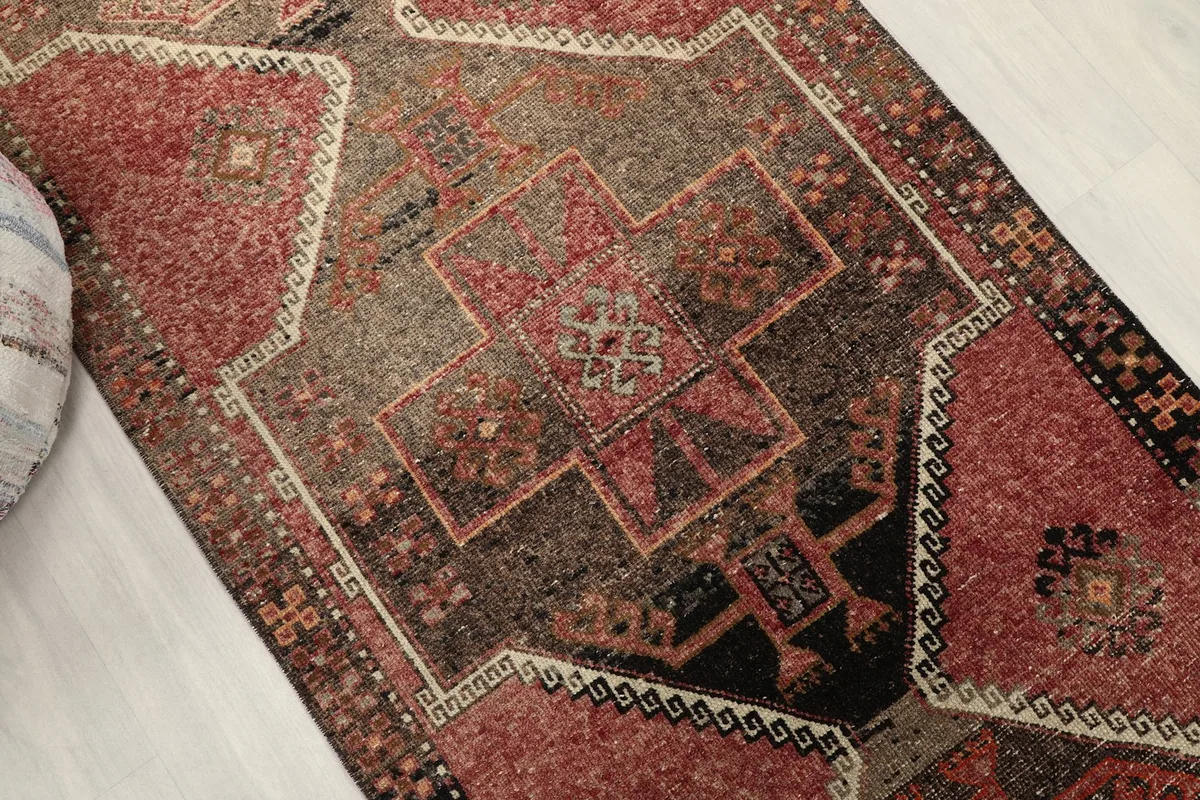 Detailed view of the rug's faded rose and brown sections with intricate tribal designs