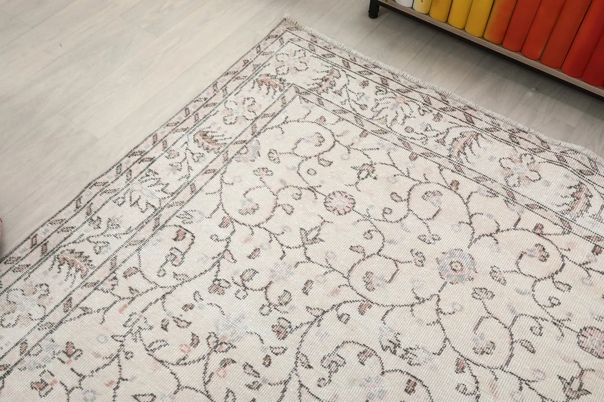 View of one end of the rug in a room, showing the border pattern and the soft color variations on the cream field.