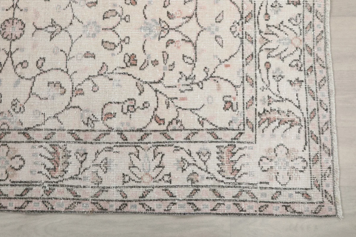 Detailed view of a corner of the rug, highlighting the intricate cream, rose, and gray floral border design.