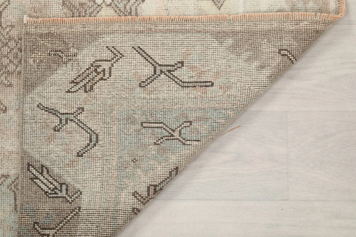 Corner of the rug flipped to reveal the hand-knotted construction and vintage wear on the reverse.