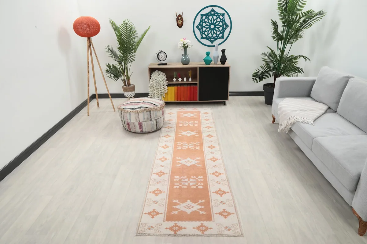 Orange and beige runner rug laid out in a modern living space with a light gray sofa and wooden cabinet.