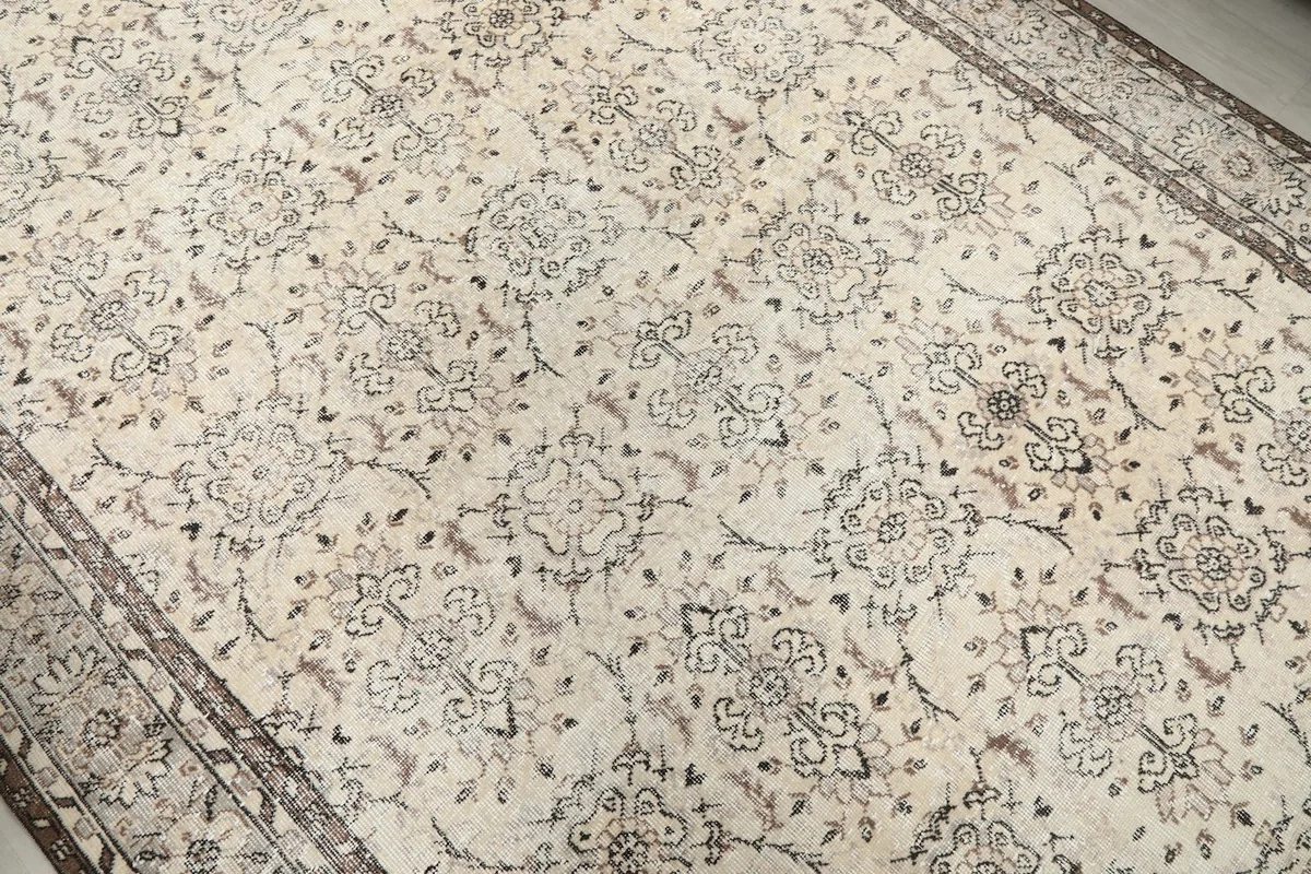 Close-up of the all-over ivory field with brown and beige floral patterns on the rug