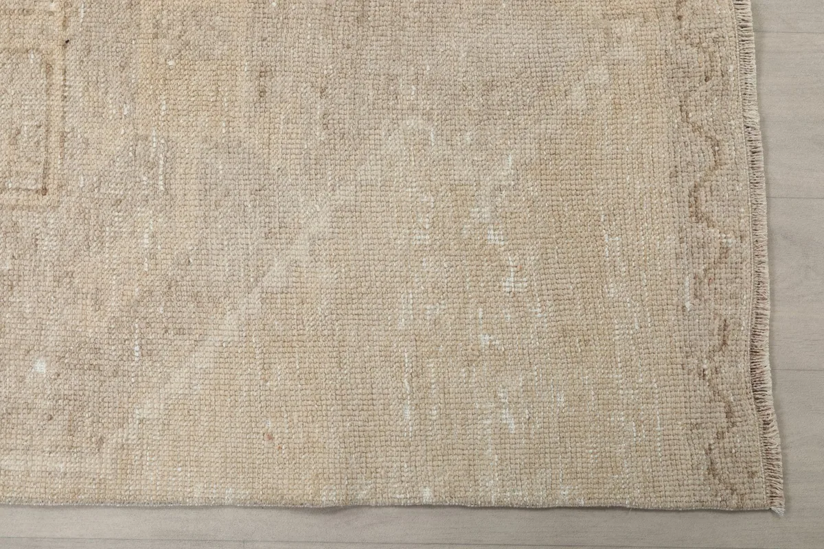 Detailed view of the rug's faded beige and tan wool pile with a subtle border design.